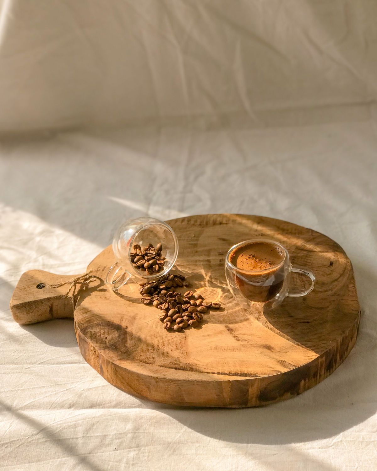 A round paddle board on linen in low sun, with a glass of coffee and spilled coffee beans